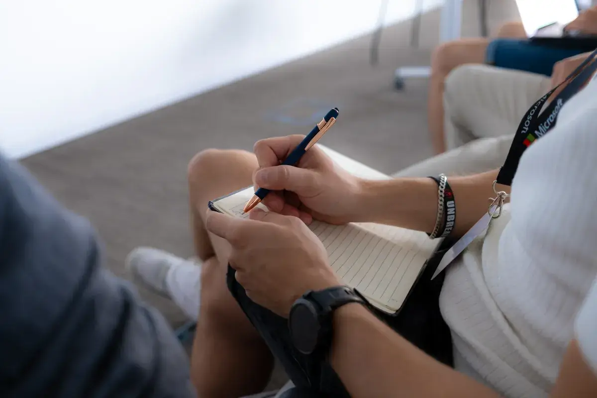 Student se šňůrkou Microsoft si během přednášky píše poznámky do zápisníku.