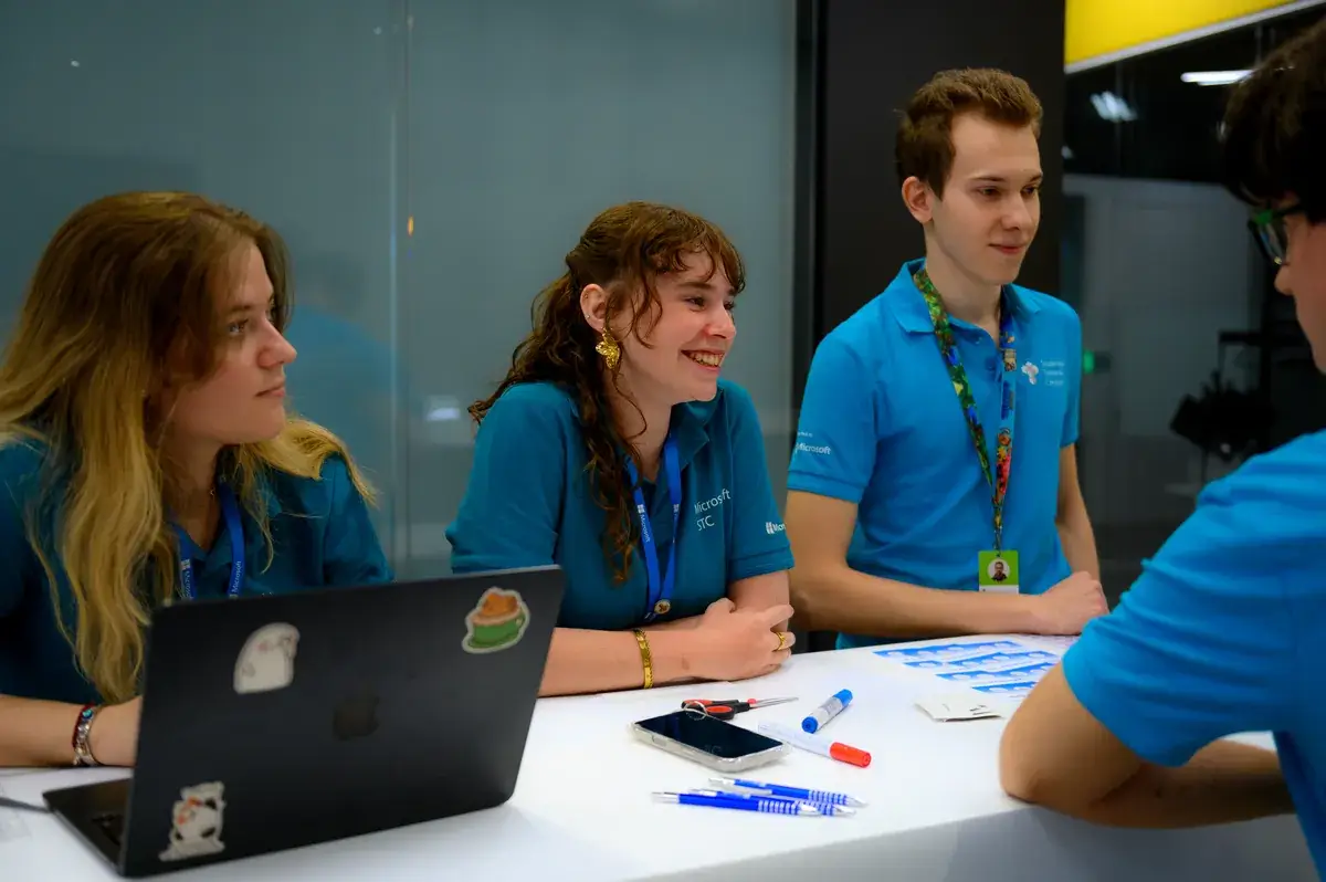 Studenti v tričkách STC sedí u stolu a usmívají se během finále výběrového řízení.
