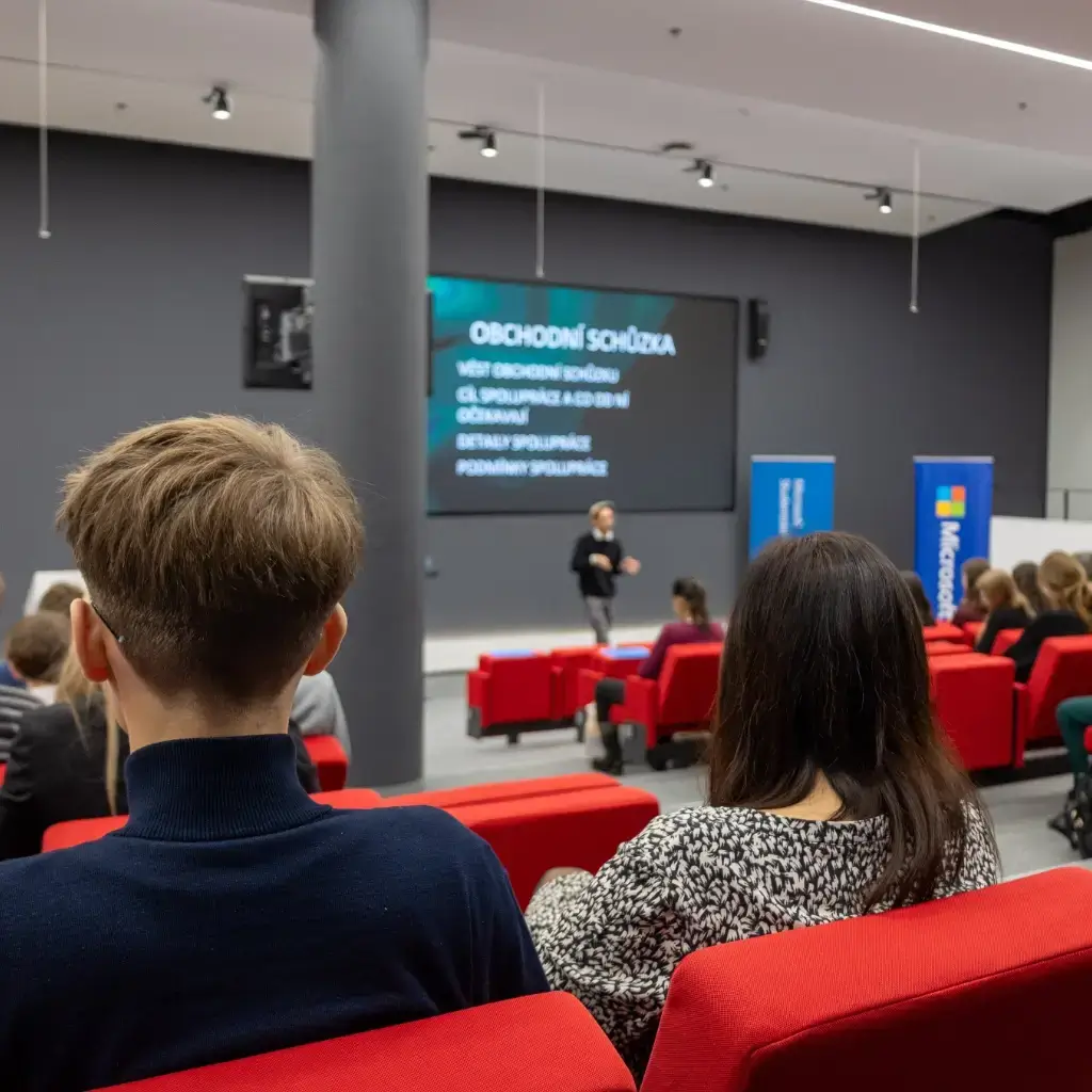 Skupina lidí sedící v sedačkách se účastní přednášky v budově Microsoftu v Praze.